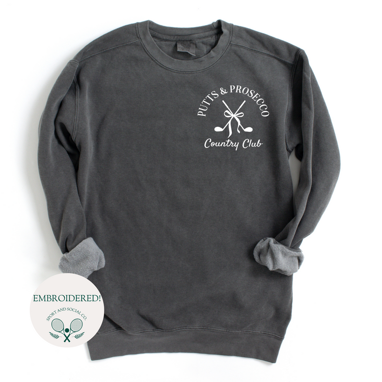 Comfort Colors mid-weight crewneck sweatshirt with 'Putts and Prosecco' embroidered in pocket position, featuring a boho-style bow and crossed golf clubs design.