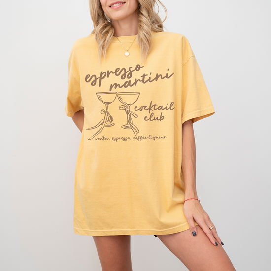 Unisex Comfort Colors short sleeve T-shirt with boho-style Espresso Martini print. Features retro martini glasses adorned with bows, in a faded vintage-inspired design on soft cotton fabric.