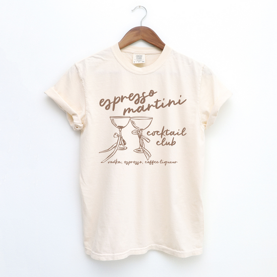 Unisex Comfort Colors short sleeve T-shirt with boho-style Espresso Martini print. Features retro martini glasses adorned with bows, in a faded vintage-inspired design on soft cotton fabric.