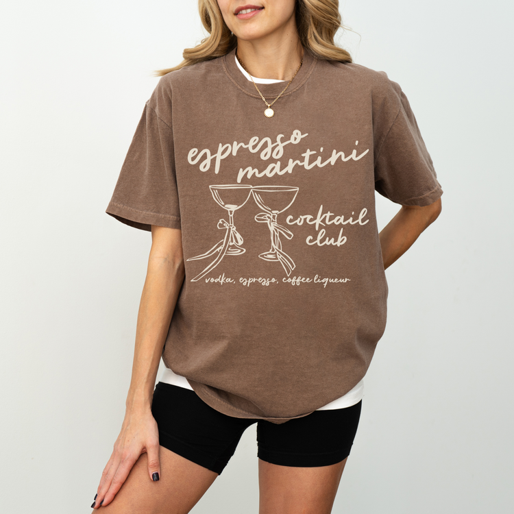 Unisex Comfort Colors short sleeve T-shirt with boho-style Espresso Martini print. Features retro martini glasses adorned with bows, in a faded vintage-inspired design on soft cotton fabric.