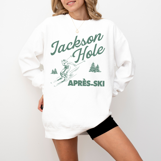 Model wearing a lightweight crewneck sweatshirt with 'Jackson Hole Après Ski' design. The back features a boho retro illustration of a woman skier, giving off relaxed and nostalgic après-ski vibes.