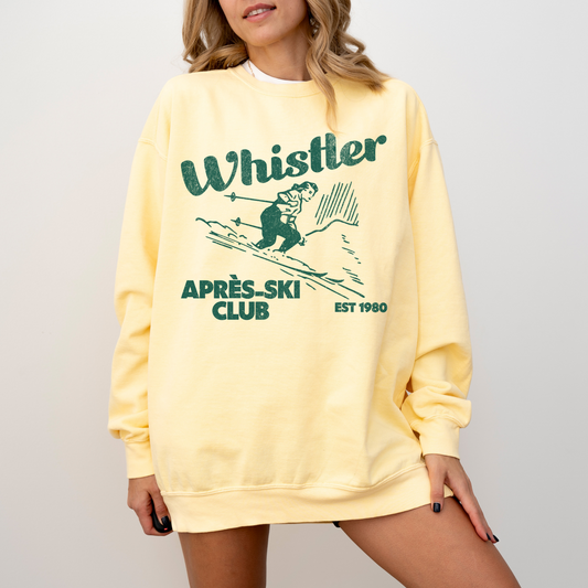 Lightweight cotton crewneck sweatshirt with "Whistler Après Ski Club" in vintage retro style, featuring a graphic of a woman skiing, perfect for après-ski and winter adventures.