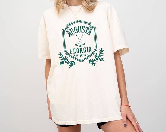 Model wearing a retro style Augusta, Georgia short sleeve t-shirt with vintage golf-inspired graphics, Ivory Color Shirt